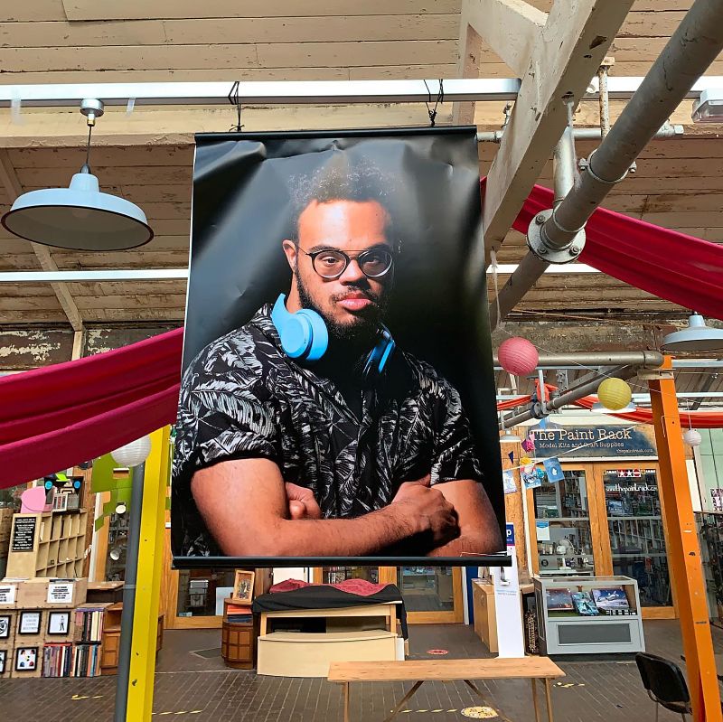 A young man with Down's Syndrome wears headphones around his neck in an exhibition image hanging in a large hall