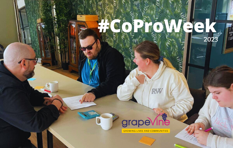 A group of four, two men and two women, sit in casual clothing around a table with coffee mugs, pens and notebooks talking about coproduction and what it means to them.