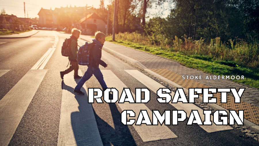 Two young boys wearing rucksacks use a zebra crossing to cross a residential road at sunset. The words say, Stoke Aldermoor Road Safety Campaign.