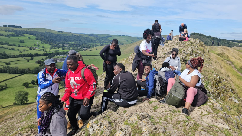 A group of black people gather at the top of a hill in the Peak District to have a rest and enjoy the view.