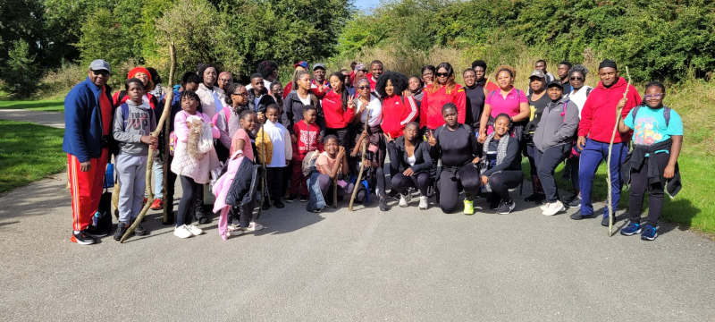 A group of around 50 black adults and children pose for a photo together to mark a walk through the Peak District on a sunny September day.